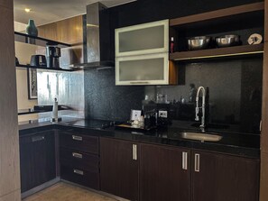 A modern kitchen with dark cabinetry, a black countertop, a stainless steel sink, and a built-in microwave. - PGA Open and Luxury Living in a 3 Bedroom Suite in sunny Mexico! (Nuevo Nayarit)