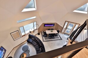Un intérieur moderne avec un canapé noir aux lignes courbes, une table à manger et un escalier.