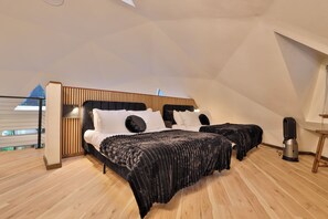 A bedroom with a sloped ceiling, a bed with a black headboard, and a wooden floor. - Hidden Dome Retreat in the Trees (Coos Bay)