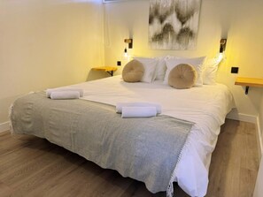 A neatly made bed with a grey blanket and two rolled towels, a wall with a textured artwork, and two bedside lamps. - Tropical Views - Playa del Inglés (Playa del Inglés)