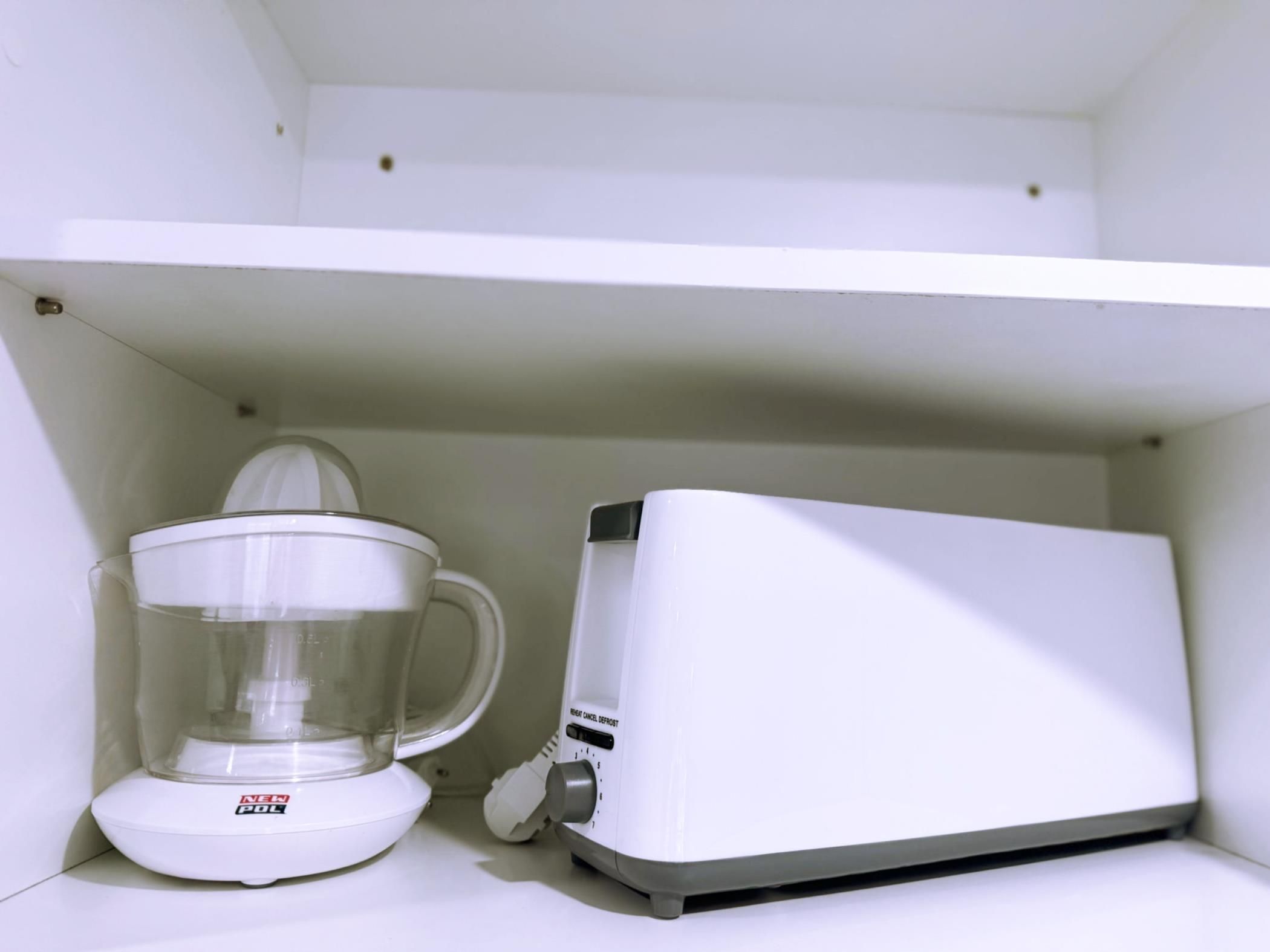 Une cuisine blanche avec une machine à café et un récipient en verre posé sur le plan de travail.