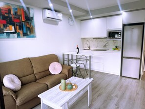 A modern living room with a brown sofa, a white coffee table, and a kitchen area with white cabinets and appliances. - Tropical Views - Playa del Inglés (Playa del Inglés)