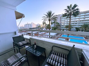 A balcony with a table, chairs, and a bottle of wine. In the background, there is a swimming pool and palm trees. - Tropical Views - Playa del Inglés (Playa del Inglés)