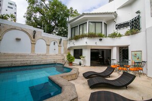 Un área de piscina con un muro de piedra, sillas de descanso y un comedor con mobiliario exterior.