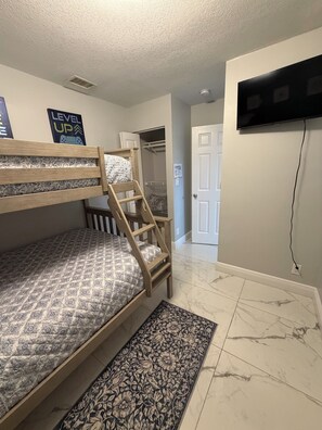A bunk bed with a patterned mattress, a wooden ladder, a patterned rug, a television mounted on the wall, and a door leading to a closet. - Roxana's Modern House (Coral Springs)