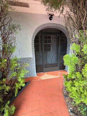 A brick pathway leading to a door with a decorative metal gate, surrounded by greenery. - Roxana's Modern House (Coral Springs)