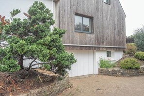 A modern building with a wooden facade, a small window, and a well-maintained garden with a coniferous tree. - Séjour nature et océan : Grande maison de famille (Guidel)