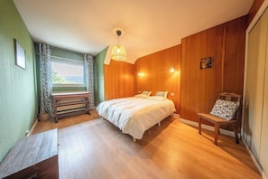 A bedroom with a bed, wooden walls, a bench, and a window with curtains. - Séjour nature et océan : Grande maison de famille (Guidel)