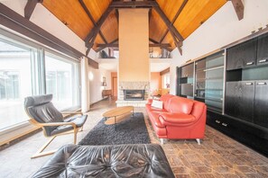 A modern living room with a fireplace, leather furniture, and a large window. - Séjour nature et océan : Grande maison de famille (Guidel)