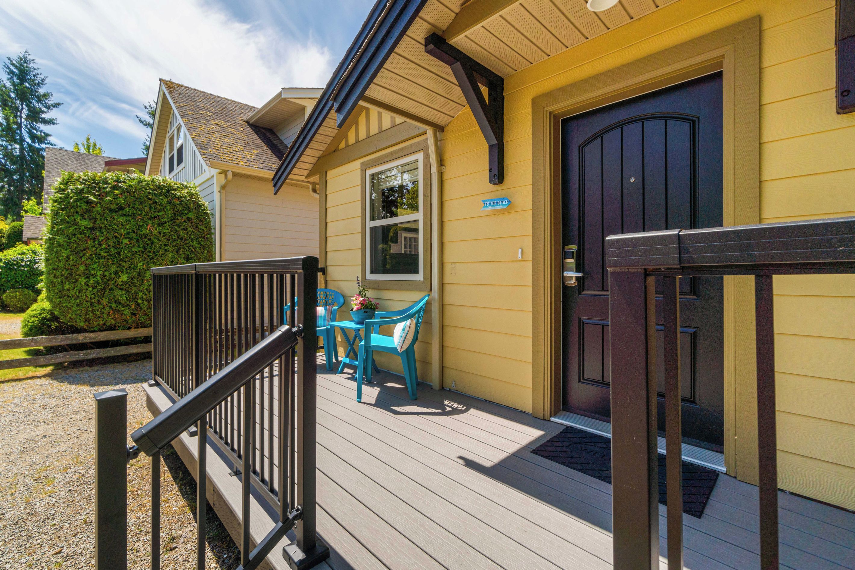A wooden deck with a black railing, a blue chair, and a table with a flower pot.