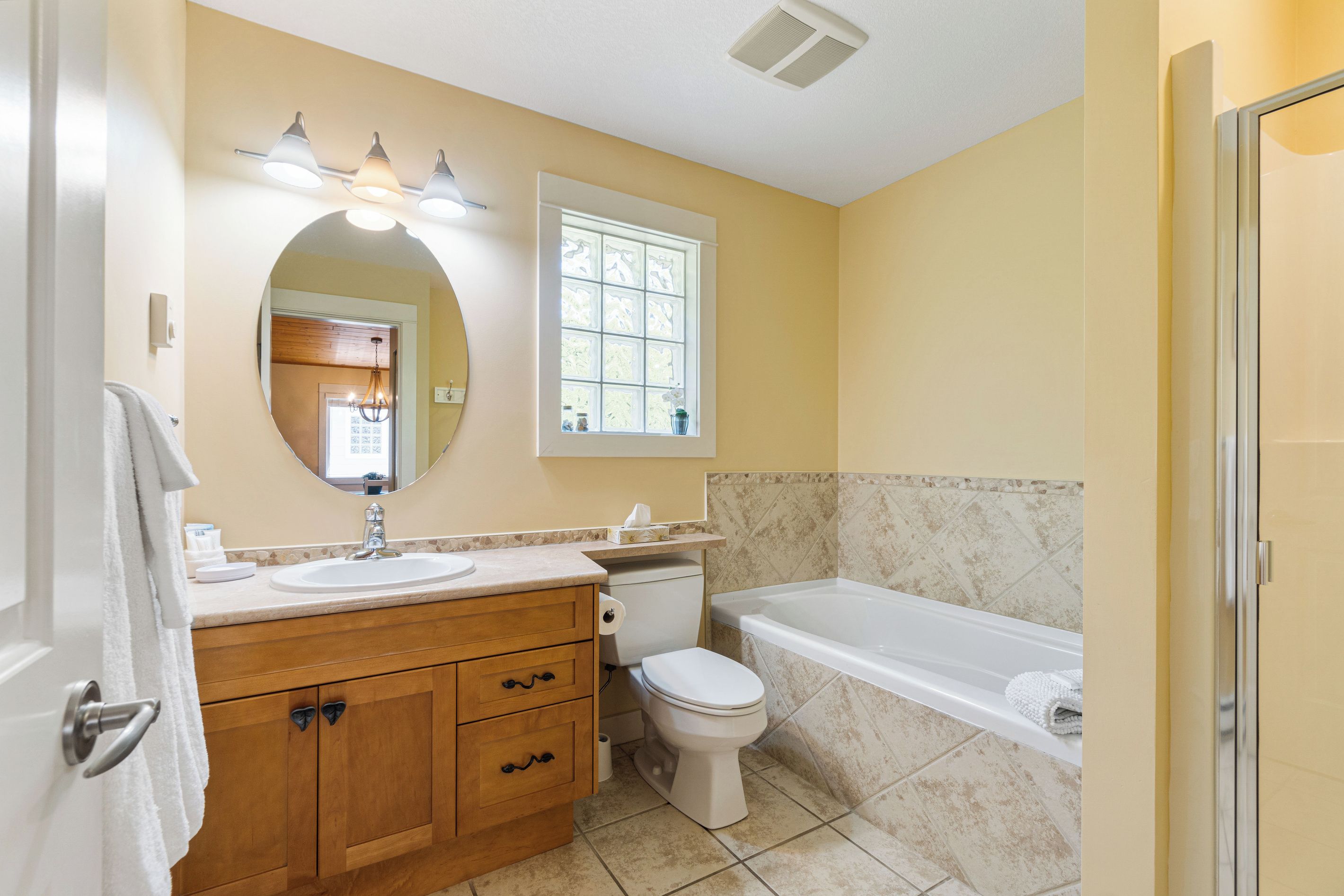 Une salle de bain avec un meuble-lavabo en bois, des toilettes, une baignoire et une fenêtre.