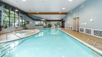 An indoor swimming pool with clear water, surrounded by windows, and equipped with safety railings.