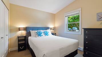 A bedroom with a bed, two bedside tables, a dresser, a window with a view of trees, and a door.