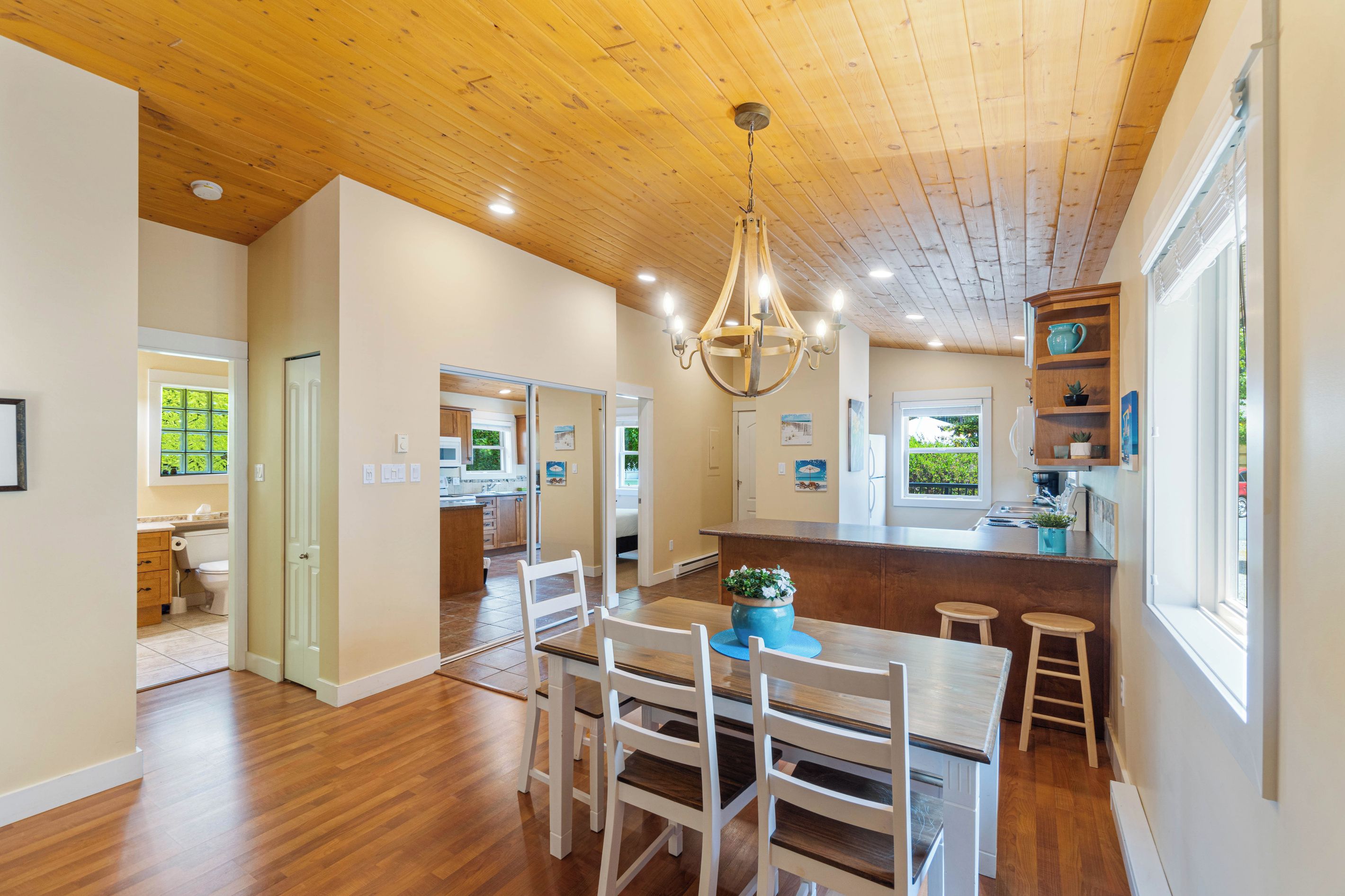 A spacious kitchen with wooden flooring, a dining area with white chairs, and a wooden ceiling.