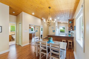 Una cocina amplia con suelo de madera, un comedor con sillas blancas y un techo de madera.