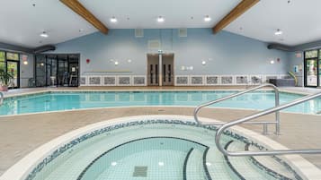 An indoor swimming pool with a tiled edge, a metal ladder, and a ceiling with wooden beams.