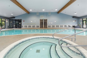 Una piscina interior con borde de azulejos, una escalera de metal y un techo de vigas de madera.