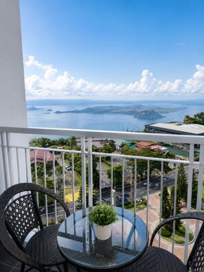 Un balcone con tavolo e sedie in vetro, con vista su un paesaggio costiero con edifici e una strada.