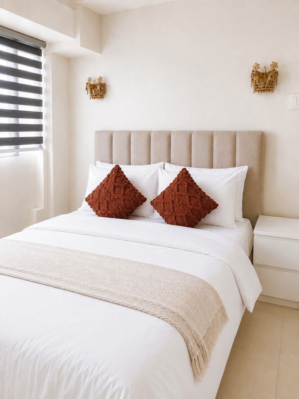 Una cama bien hecha con cabecera, dos almohadas y una colcha.