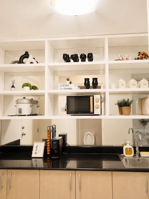 Una cocina con estanterías blancas, una encimera negra y diversos electrodomésticos.