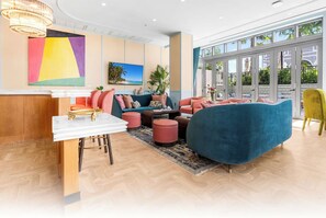 A modern lounge area with a marble reception desk, plush seating, and large windows offering a view of the outdoors. - NoMad Residences Wynwood Private Luxury Suites (Miami)