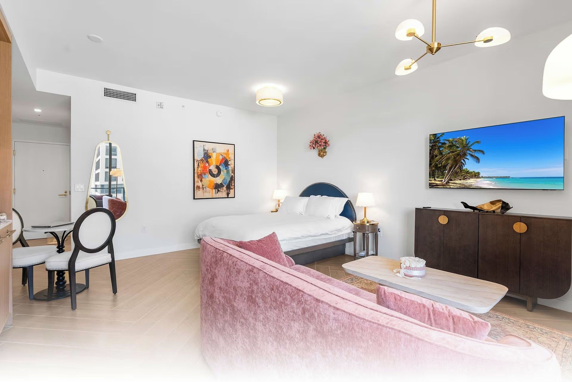 A modern bedroom with a bed, bedside tables, a dresser, a seating area, and a television on the wall.