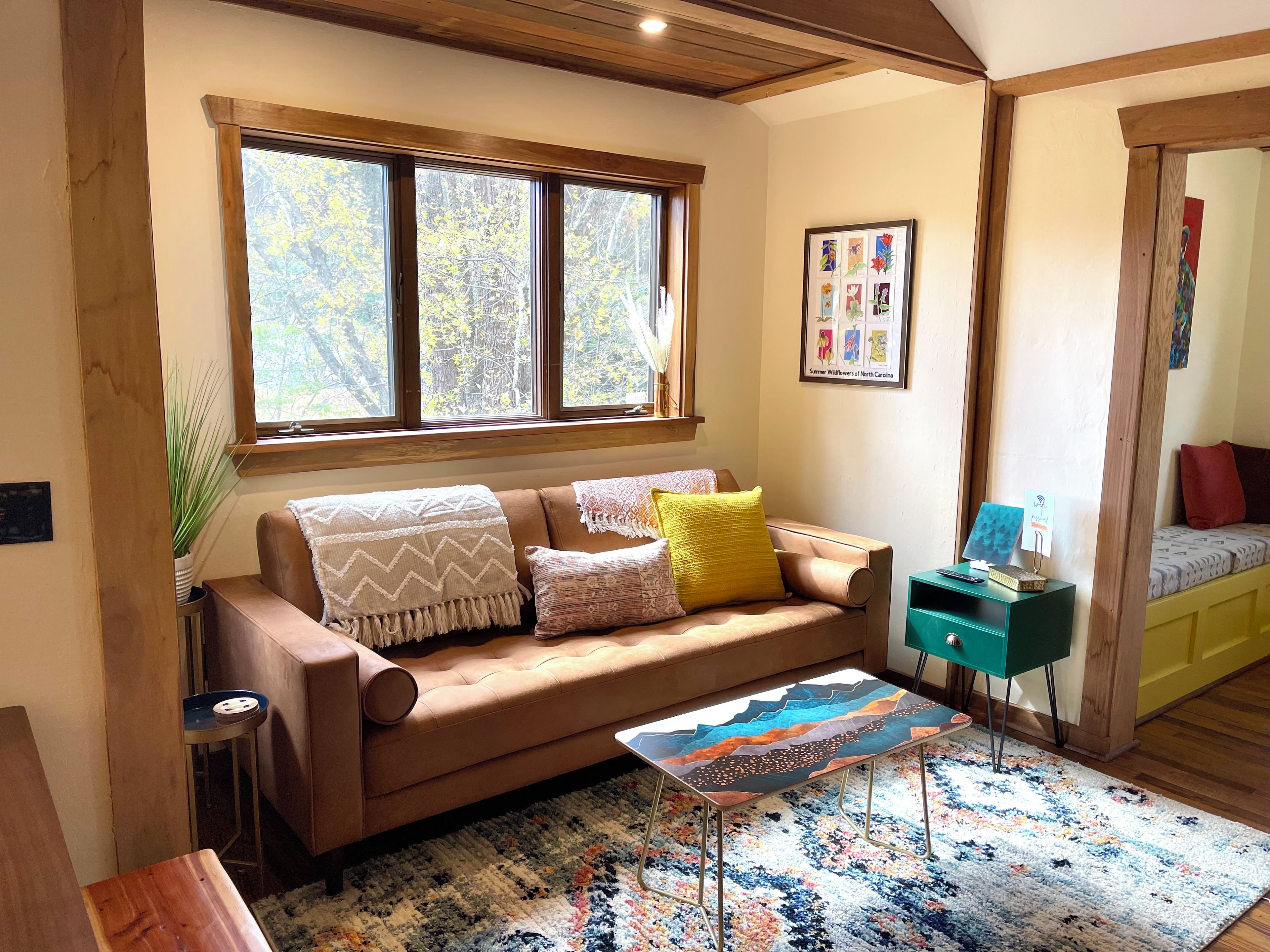 A cozy living room with a brown leather sofa, a colorful rug, and a wooden ceiling.