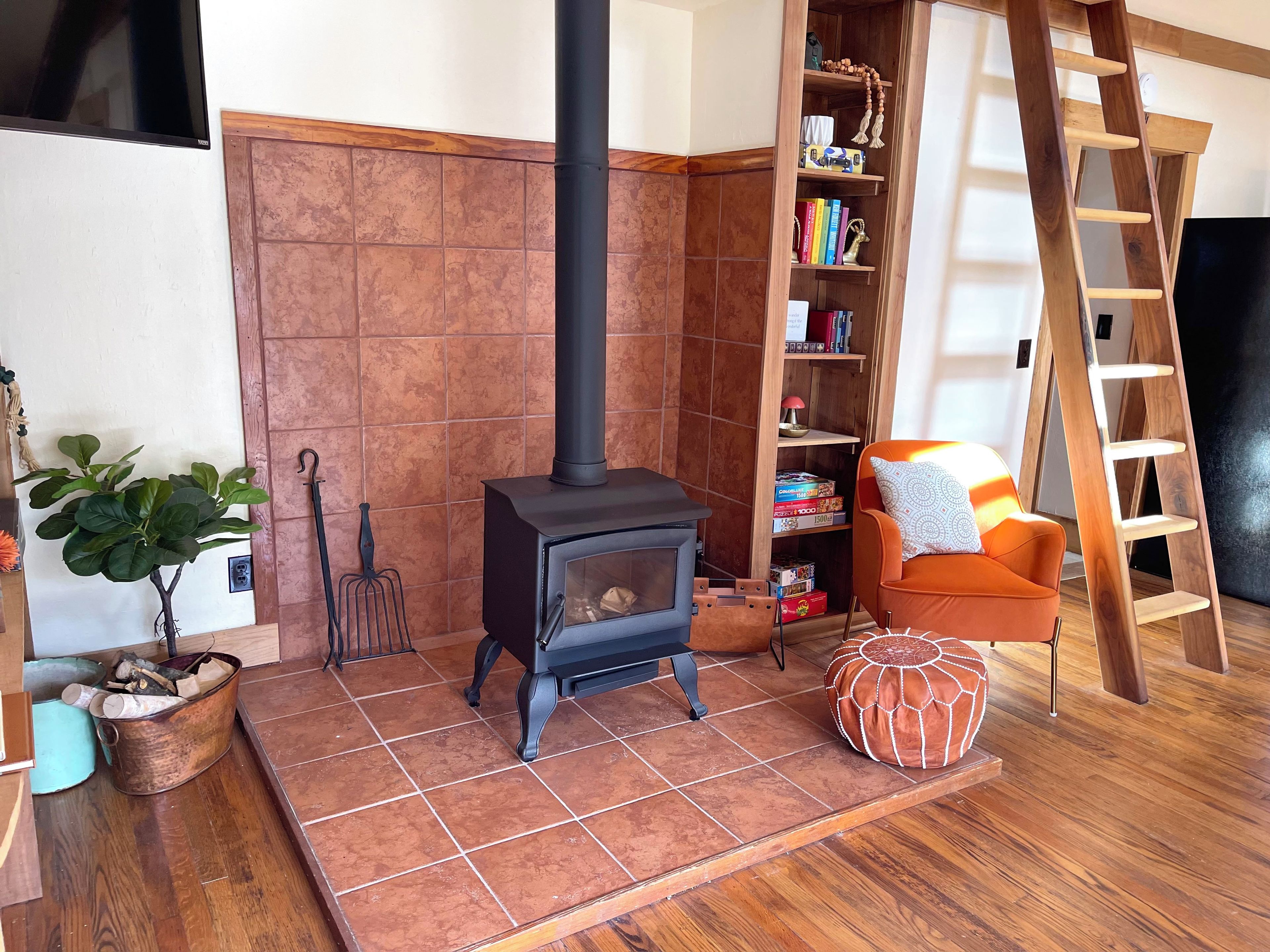 Una habitación acogedora con una estufa de leña, una estantería, una escalera y una zona de estar confortable.