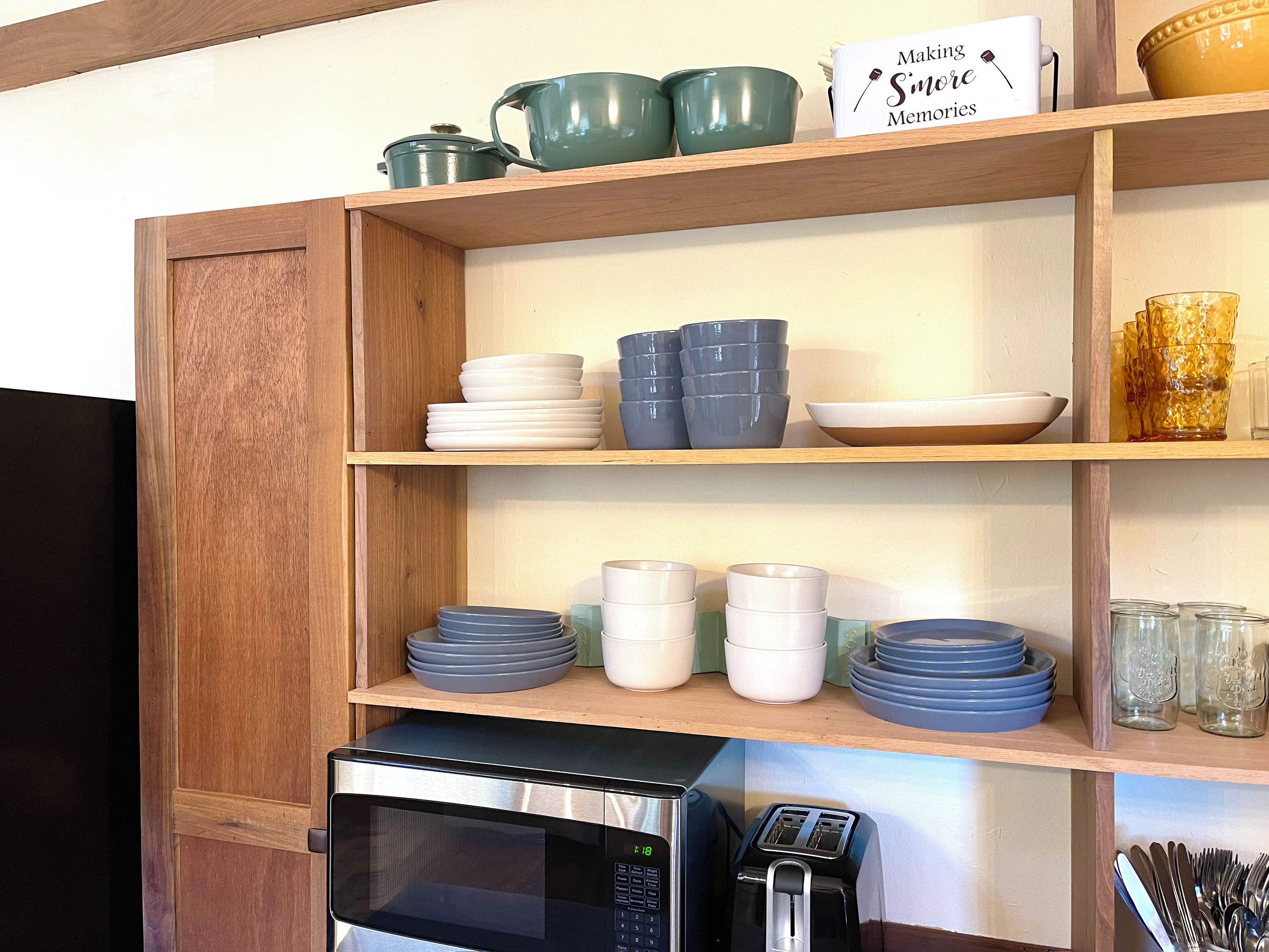 Una cocina con estantes de madera que exhiben diversos utensilios y un microondas.