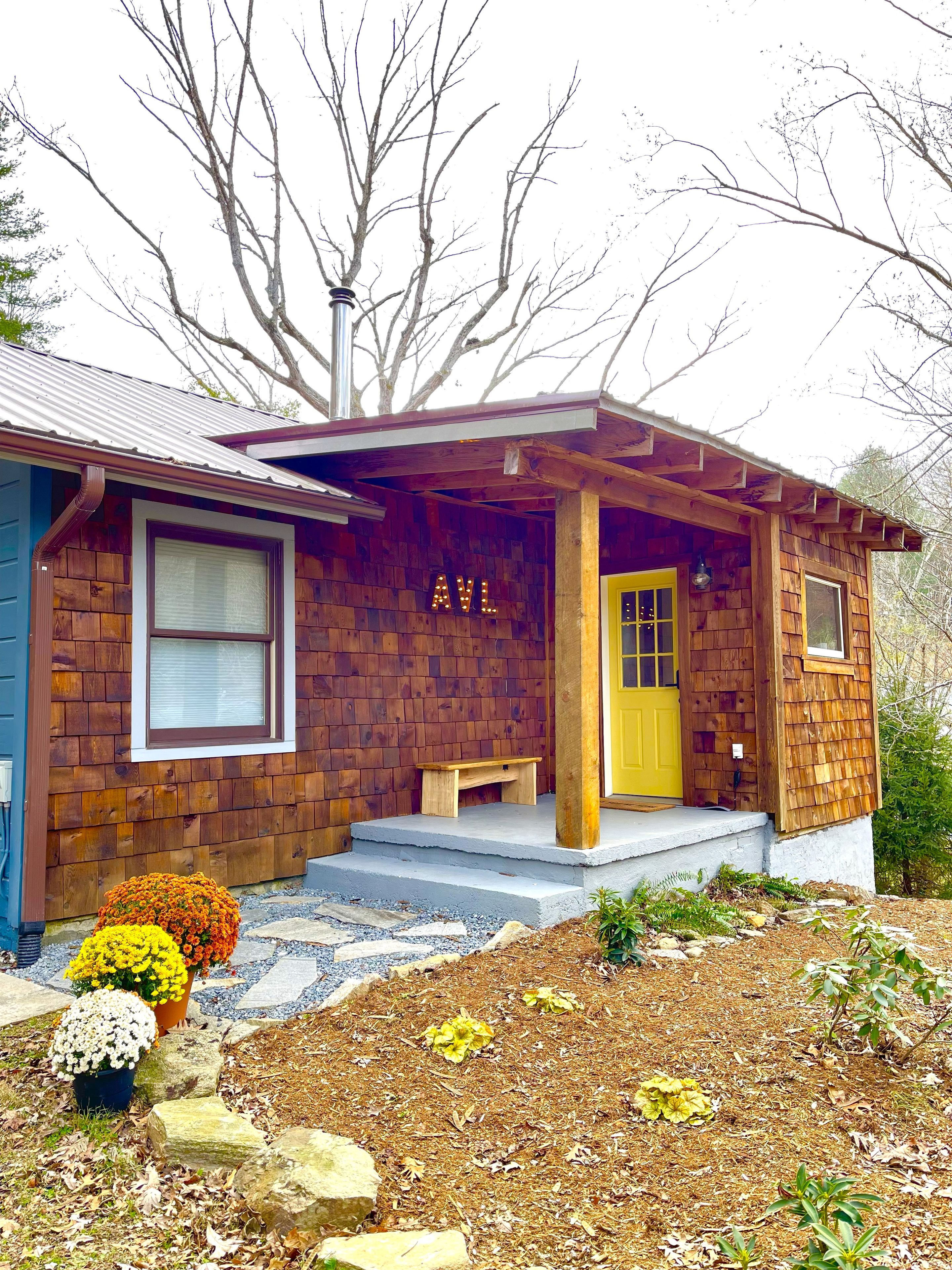 A wooden cabin with a porch, a yellow door, and a bench.