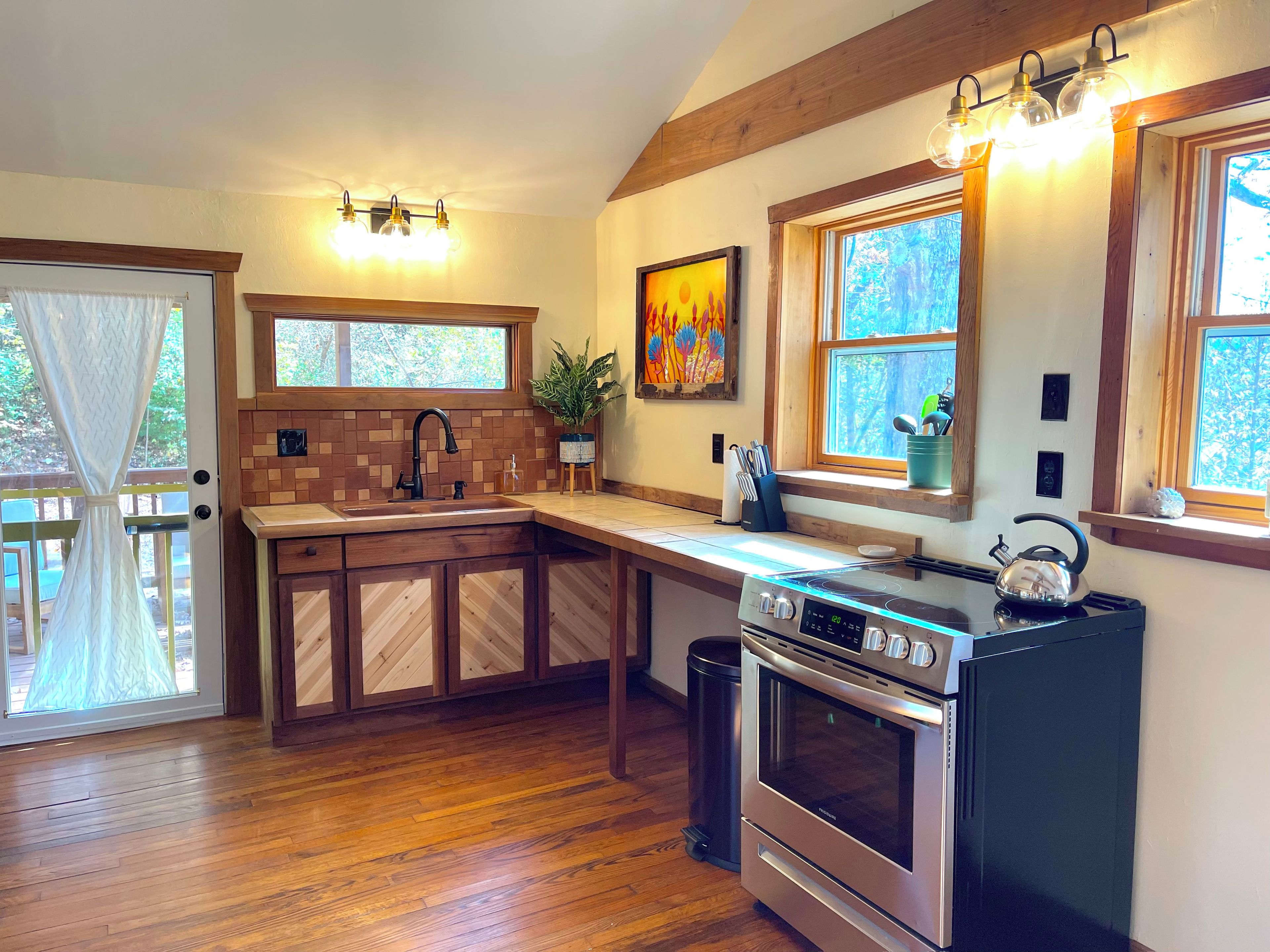 A kitchen with wooden cabinets, a stainless steel stove, and a window with a view of trees.
