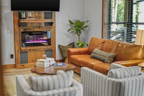A cozy living room with a fireplace, leather sofa, striped armchairs, and a coffee table. - Sleeps 12, Game Room with Arcade, Air Hockey, PS5, Hot Tub (Sevierville)