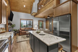Une cuisine moderne dotée d’un grand îlot central, d’appareils électroménagers en acier inoxydable et de meubles de rangement en bois.