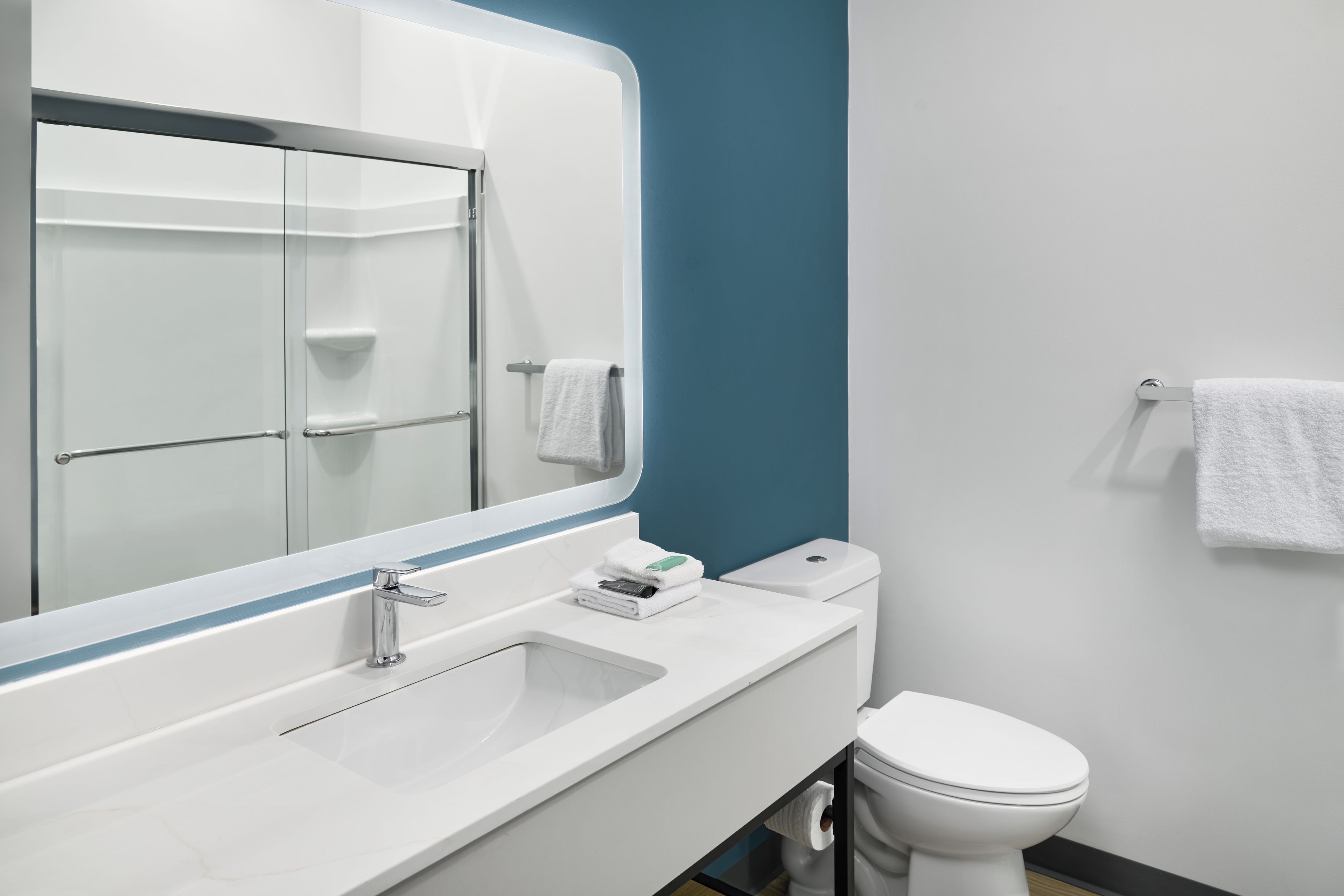A modern bathroom with a white sink, a mirror, a toilet, and a towel rack.