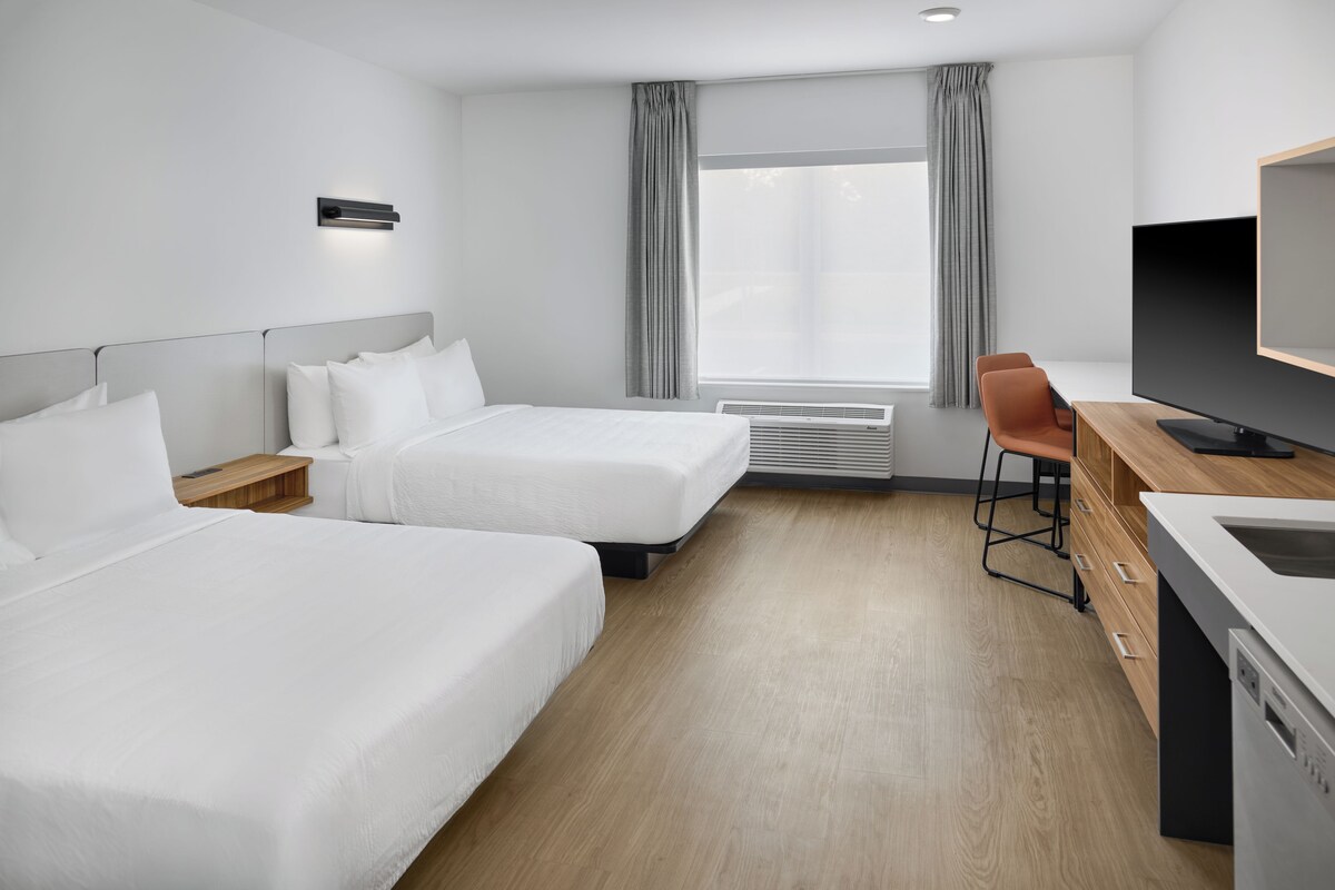 A hotel room with two beds, a desk with a television, and a window with curtains.