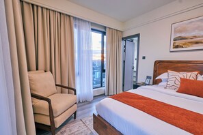 A hotel room with a bed, a chair, a window with curtains, and a painting on the wall. - 16th Floor Luxury -GTC Skyline Views with gym and workspace (Nairobi)