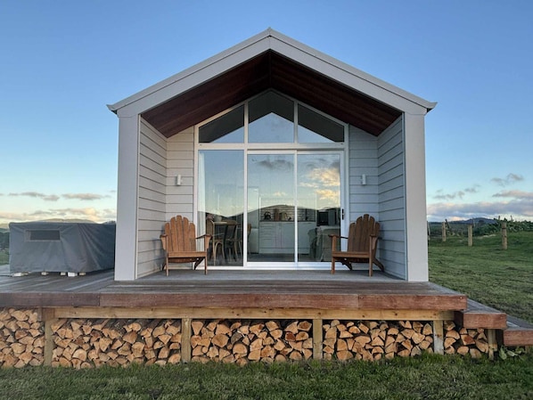 A small cabin with a porch, wooden chairs, and a glass door leading inside.