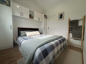 A bedroom with a bed, a wardrobe, a nightstand, and a wooden ladder.