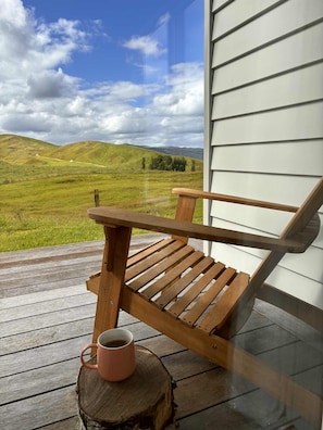 A wooden chair on a wooden deck with a view of a green landscape and hills.