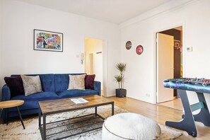 A living room with a blue sofa, a coffee table, a foosball table, and a potted plant. - Design-Led Shoreditch Flat | Graffiti • Brick Lane (Greater London)