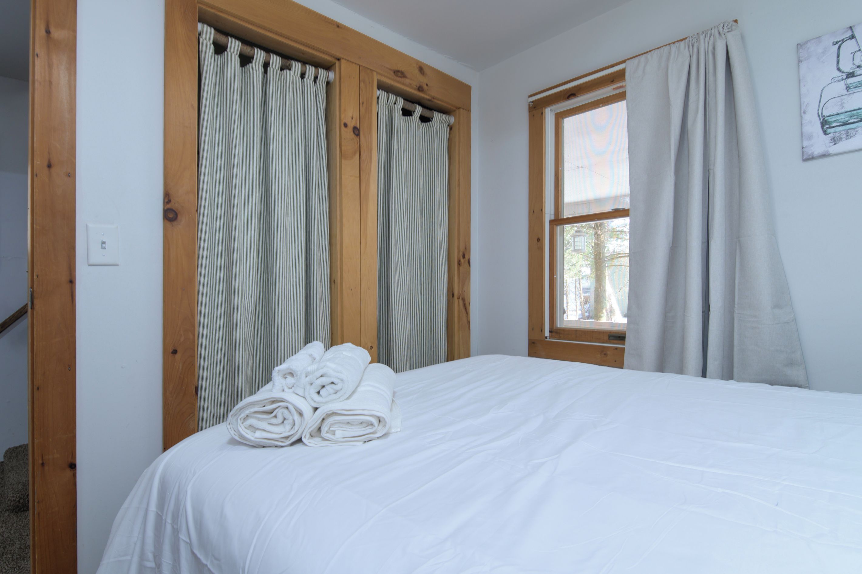A bedroom with a bed, wooden window frames, and curtains.