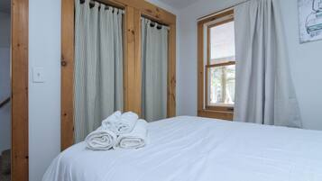 A bedroom with a bed, wooden window frames, and curtains.
