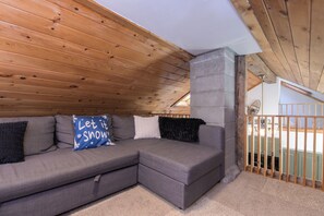 A wooden ceiling, a grey sectional sofa with pillows, and a concrete pillar. - Historic 1880s Cape, 10 Min to Jay Peak | Rustic Charm, Clawfoot Tub & Workspace (Montgomery Center)