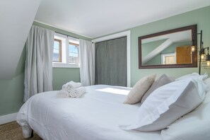 A hotel room with a bed, white linens, a window with curtains, a mirror, and a light fixture.