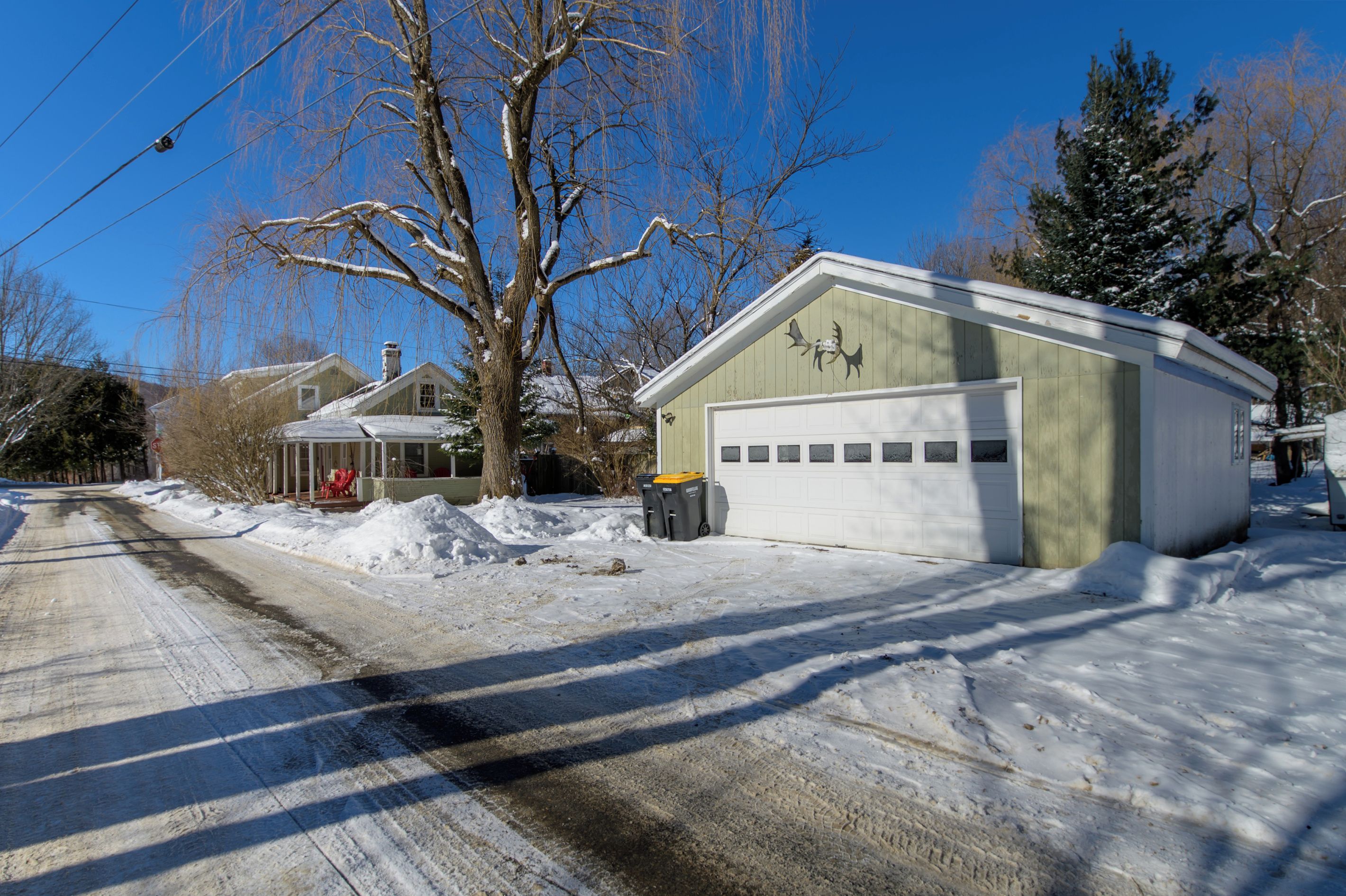 A residential area with a garage, a covered porch, and a snow-covered road.