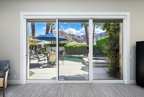 Ein Zimmer mit einer Schiebeglastür, die auf eine Außenpatio mit Pool, Stühlen und Sonnenschirmen führt.