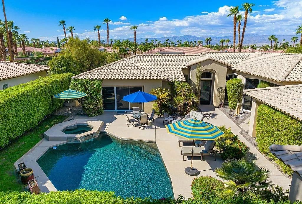 A residential property with a swimming pool, patio furniture, and a view of palm trees and mountains.