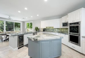 A modern kitchen with white cabinetry, a large island with a marble countertop, built-in appliances, and a view of the outdoors. - Soothing 3-bedroom /4bath house less than 1 mile from WTA Finals Indian Wells (Indian Wells)