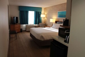 Una habitación de hotel con cama, escritorio, televisión, lámpara y un cuadro en la pared.