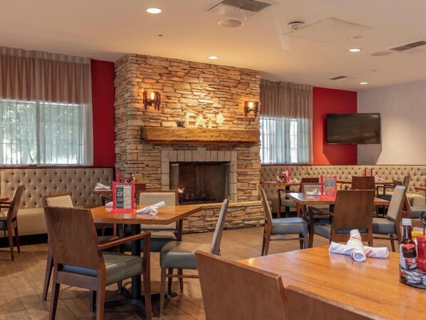 Un restaurante con chimenea de piedra, asientos acolchados y un televisor de pantalla plana en la pared.